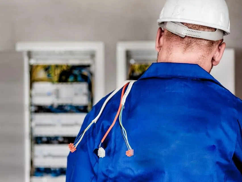 Electrician in a hard hat working at an open electrical panel